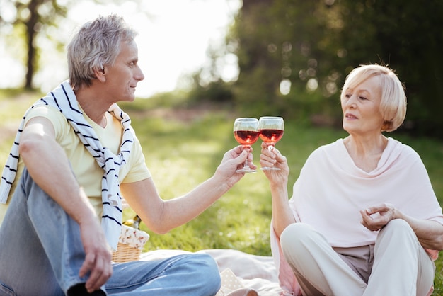 Spokojna, kochająca para seniorów, wyrażająca miłość, ciesząc się piknikiem i pijąc wino