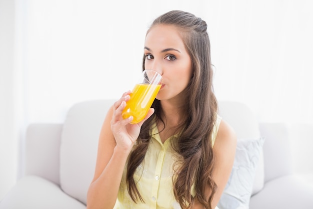 Spokojna młoda brunetka pije szkło sok pomarańczowy