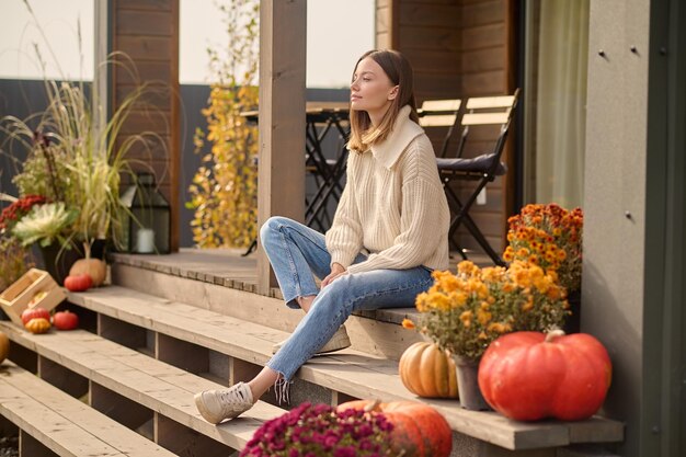 Spokojna młoda kobieta siedzi samotnie na drewnianym ganku domku i patrzy w dal