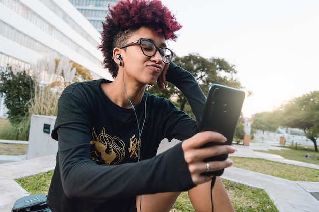 Spokojna młoda kobieta w parku ze słuchawkami i telefonem podczas wideorozmowy ze swoim chłopakiem