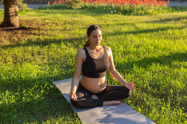 Spokojna młoda pozytywna kobieta w ciąży w kostiumie gimnastycznym ćwiczy jogę i medytuje na macie