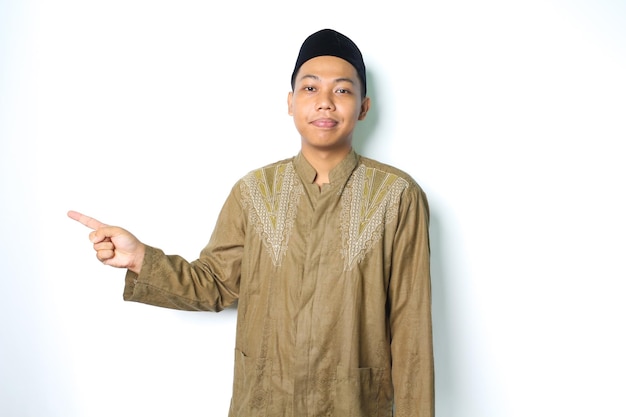 spokojny azjatycki muzułmanin uśmiecha się do kamery w ubraniach koko, wskazując obok odizolowanego na białym tle