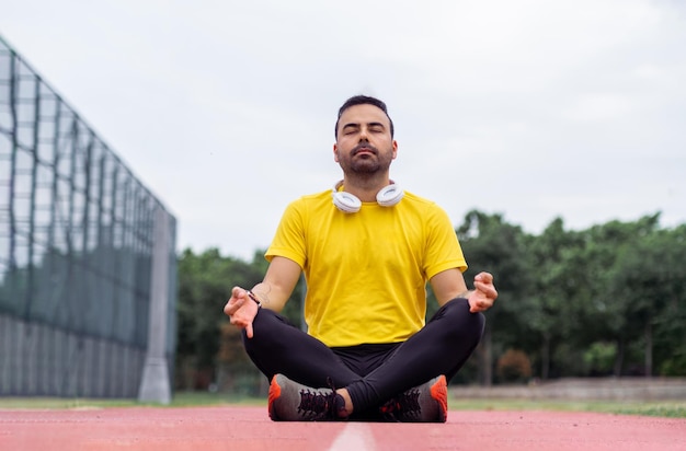 Spokojny sportowiec w tętniącej życiem odzieży sportowej medytuje w pozie lotosu na bieżni