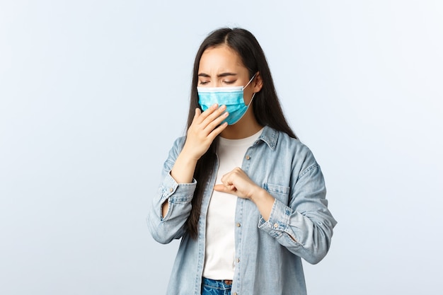 Społeczny dystansowy styl życia, pandemia Covid-19, codzienność i koncepcja wypoczynku. Azjatycka dziewczyna z pozytywnym wynikiem testu na koronawirusa, nosząca maskę medyczną i kaszle, jest chora na zamknięcie.
