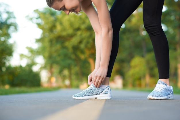 Sport dziewczyna wiąże sznurówki na torze wyścigowym parku.