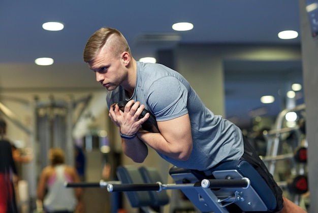 sport, fitness, kulturystyka, styl życia i koncepcja ludzi - młody człowiek napina mięśnie pleców i brzucha na ławce w siłowni