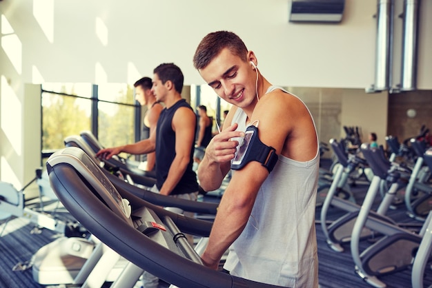 sport, fitness, styl życia, technologia i koncepcja ludzi - mężczyzna ze smartfonem i słuchawkami ćwiczący na bieżni w siłowni