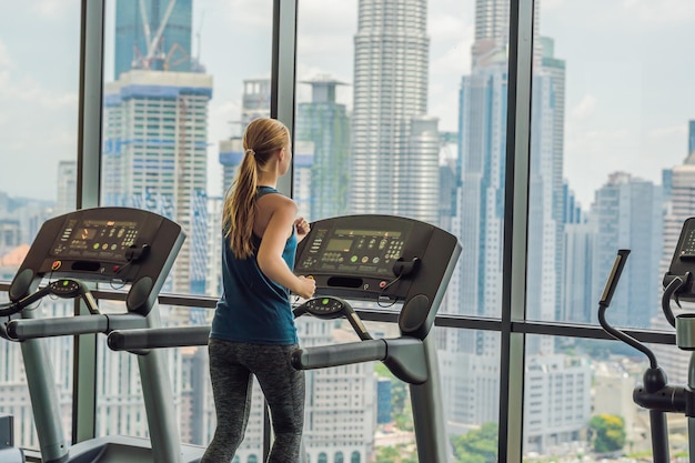 Sport fitness styl życia technologia i ludzie koncepcja kobieta ćwicząca na bieżni w siłowni na tle wielkiego miasta