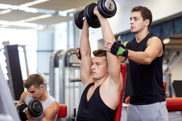 sport, fitness, styl życia, trójbój siłowy i koncepcja ludzi - grupa mężczyzn z hantlami i osobistym trenerem napinającym mięśnie na siłowni
