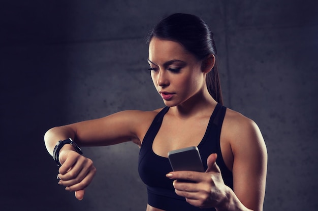 sport, fitness, technologia i koncepcja ludzi - młoda kobieta z zegarkiem do pomiaru tętna i smartfonem na siłowni