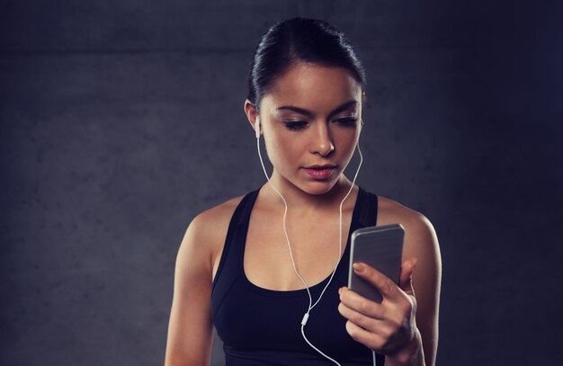 sport, fitness, technologia i koncepcja ludzi - młoda kobieta ze smartfonem i słuchawkami słuchająca muzyki na siłowni