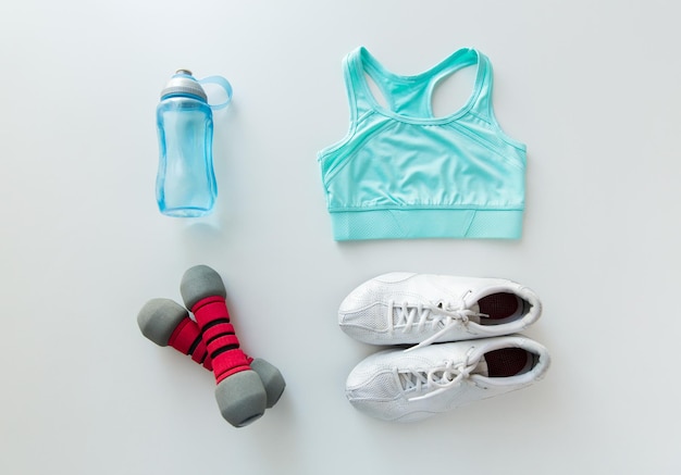 sport, fitness, zdrowy styl życia i koncepcja przedmiotów - zbliżenie kobiecej odzieży sportowej, hantli i zestawu butelek