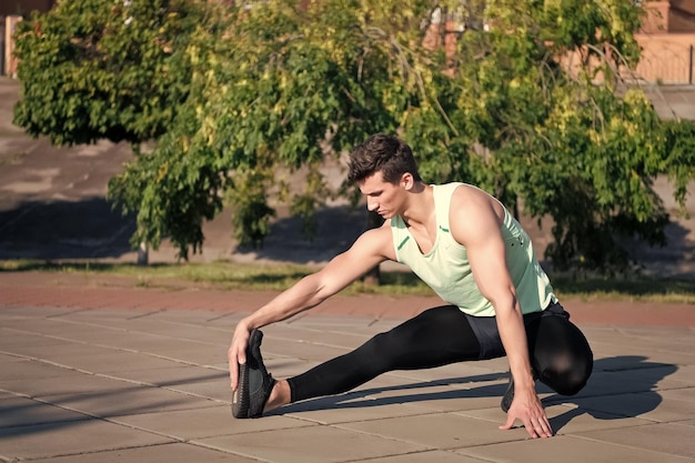 Sport i fitness Koncepcja zdrowego stylu życia Dopasuj macho w dresie na miejskim krajobrazie Mężczyzna rozciągający i rozgrzewający mięśnie przed treningiem Trening sportowca w słoneczny letni dzień na świeżym powietrzu