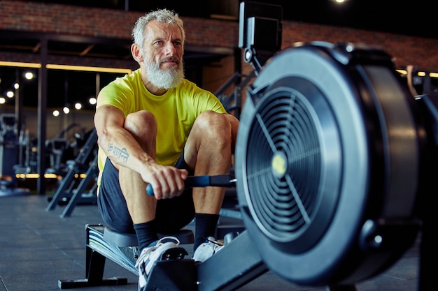 Sport i fitness po silnym dojrzałym atletycznym mężczyźnie w stroju sportowym ćwiczącym na maszynie do wiosłowania w