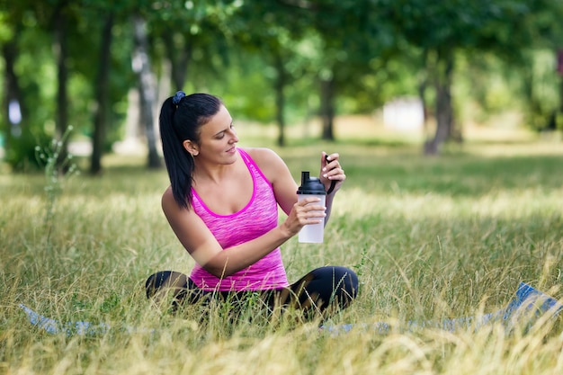 Sport kobieta trzyma wodnego obsiadanie na dywaniku w parku
