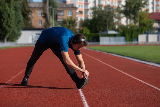 Sportive Młody Człowiek Nosi Słuchawki Robi Rozciąganie Na Bieżni. Pusta Przestrzeń