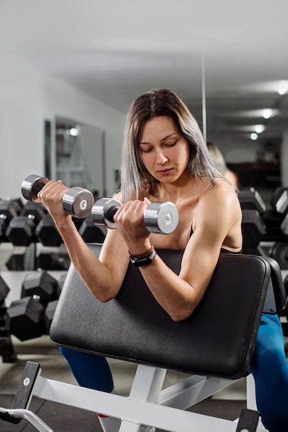 Sportowa dziewczyna fitness robi ćwiczenia z hantlami na siłowni