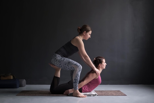 Sportowa dziewczyna jogi pomaga swojej przyjaciółce zrobić bhudjangasana lub Cobra Pose