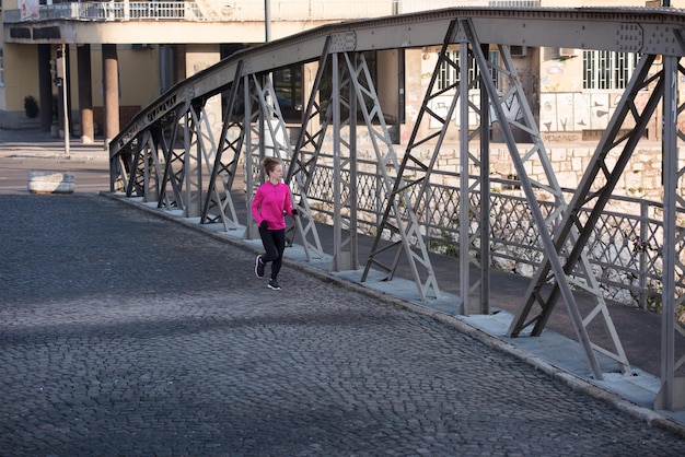 sportowa kobieta biegająca po chodniku wczesnym rankiem jogging z sceną wschodu miasta w tle