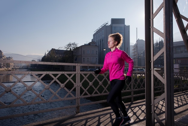 sportowa kobieta biegająca po chodniku wczesnym rankiem jogging z sceną wschodu miasta w tle