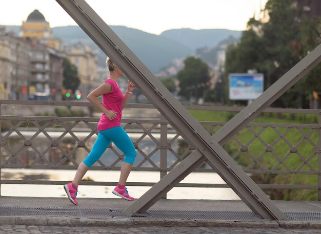 sportowa kobieta biegająca po chodniku wczesnym rankiem ze sceną wschodu miasta w tle