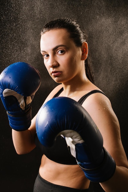 Sportowa kobieta bokserka w niebieskich rękawicach bokserskich na ciemnym tle