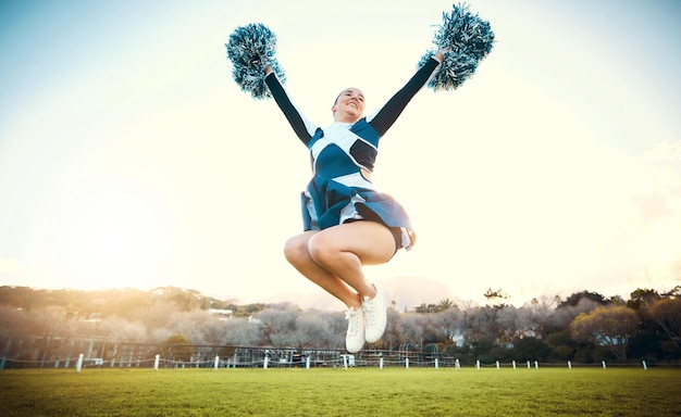 Sportowa kobieta niebo i cheerleaderka skaczą z energią, aby świętować cel na świeżym powietrzu Cheerleaderka lub sportowiec tańczy w naturze z pomponami do gry wydajności lub zawodów na zielonym polu trawy