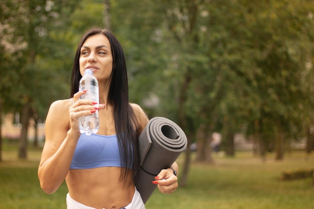 Sportowa kobieta odpoczywa po joggingu i pije wodę, trzymając w ręku butelkę