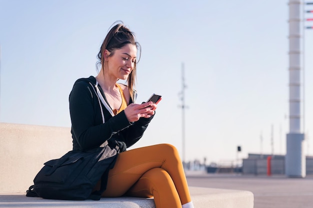 Sportowa kobieta siedzi w mieście za pomocą telefonu komórkowego
