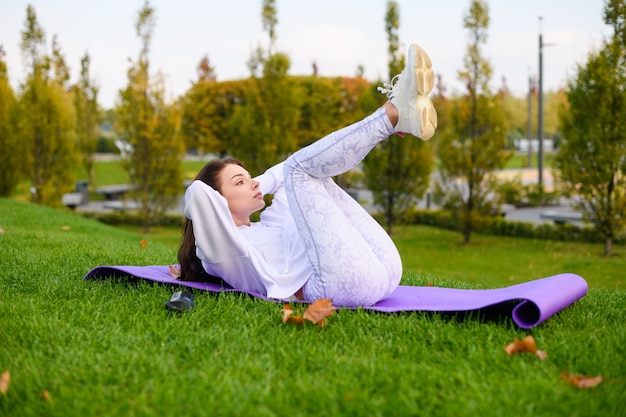 Sportowa Kobieta W Białych Ubraniach Leżała Na Macie Na Zewnątrz I Sprawiała, że Rozciąganie, Fitness, Abs Chrupie Na Tle Przyrody