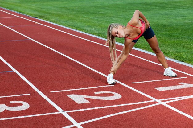 Sportowa kobieta w sportowym garniturze robi ćwiczenia treningowe przed bieganiem