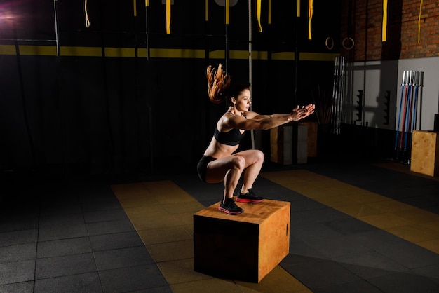 Sportowa kobieta w stroju sportowym skacząca na boksie crossfit w siłowni