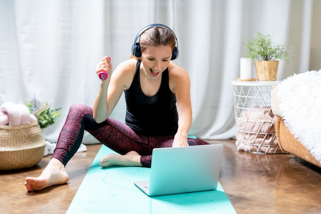 Zdjęcie sportowa kobieta ze słuchawkami na korzystanie z laptopa podczas treningu w domu.