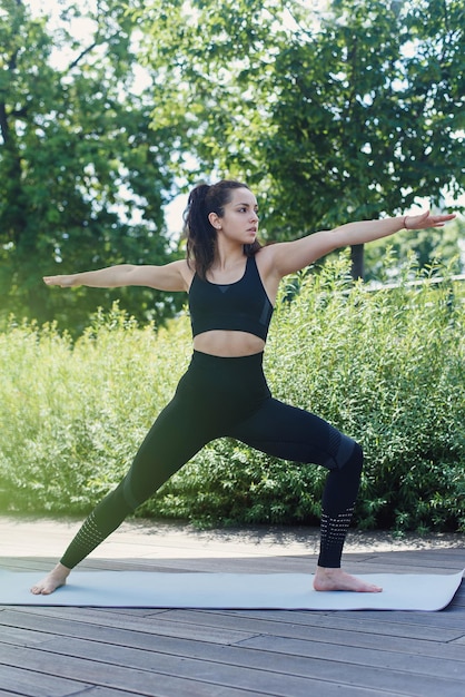 Sportowa młoda kobieta sprawia, że ćwiczenia jogi z matą do jogi w koncepcji aktywnego stylu życia na świeżym powietrzu w parku