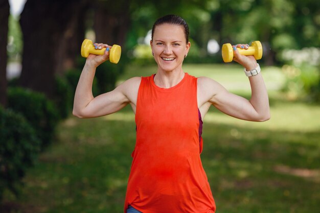 Sportowa młoda kobieta z hantlami na zewnątrz robi fit aktywność i trening na zielonej trawie w parku Sport fitness i zdrowy styl życia