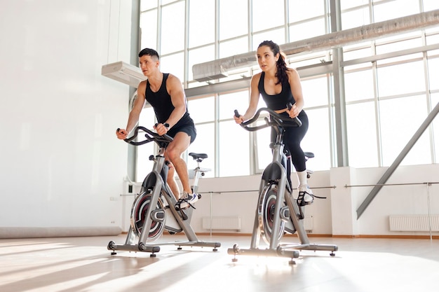 Sportowa para rowerzystów trenuje na statycznym symulatorze rowerowym, trenerze i kobiecie fitness
