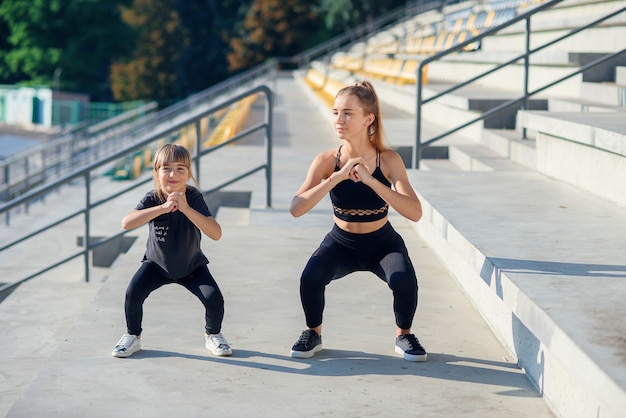 Sportowa Piękna Starsza I Młodsza Siostra, Które Przysiadują Razem Podczas Treningu Fitness Na świeżym Powietrzu.