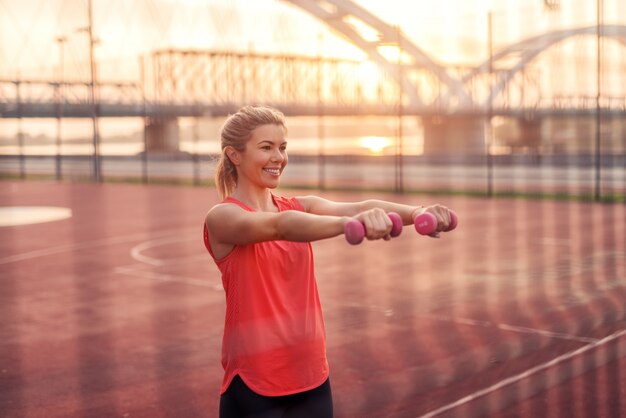 Sportowa, silnie zmotywowana blond dziewczyna trzyma ciężary.