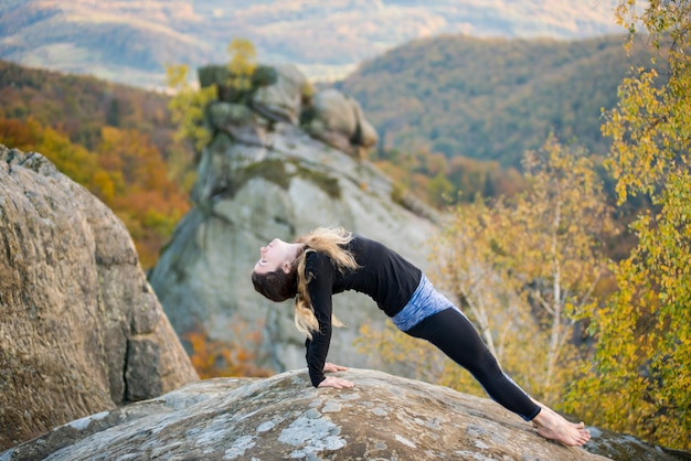 Sportowa sprawna kobieta ćwiczy jogę na szczycie góry