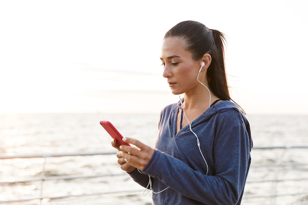 Sportowe kobiety na zewnątrz na plaży słuchanie muzyki w słuchawkach przy użyciu telefonu komórkowego.