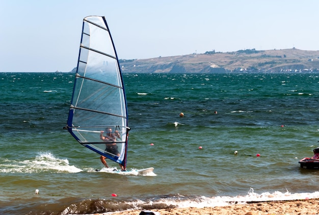 Sportowiec jadący windsurferem podpływa nad brzeg morza