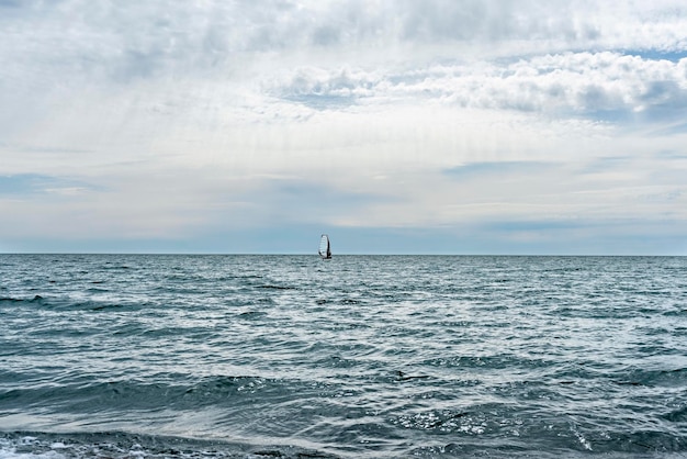 Sportowiec jedzie na windsurfingu w oddali na błękitnym morzu na tle błękitnego pochmurnego nieba latem