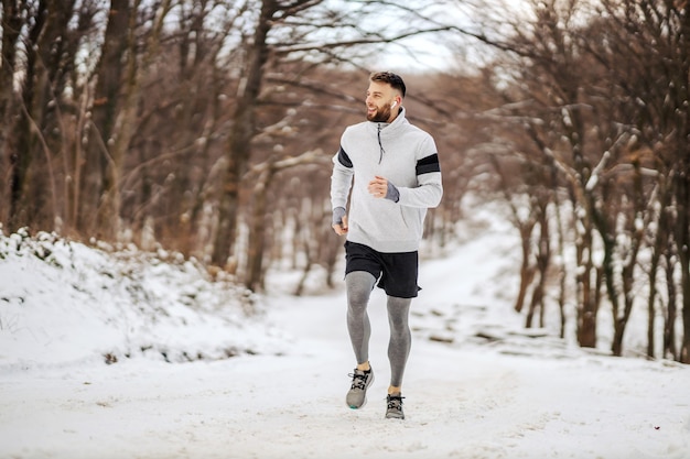 Sportowiec jogging na zaśnieżonej ścieżce w lesie w zimie. Sporty zimowe, zdrowe nawyki, outdoor