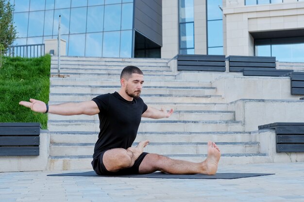 Sportowiec mężczyzna w czarnej odzieży sportowej ćwiczy ćwiczenia jogi, stretching, fitness, pozycję lotosu, pozycję wojownika.