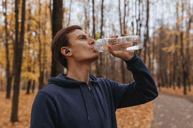 Sportowiec pije wodę z plastikowej butelki wielokrotnego użytku podczas przerwy podczas treningu w parku