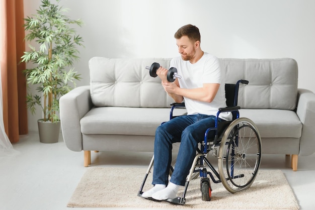 Sportowiec siedzi na wózku inwalidzkim i wyciąga ręce z hantlami podczas ćwiczeń rehabilitacyjnych w nowoczesnym centrum medycznym Mężczyzna siedzący na wózku inwalidzkim w domu