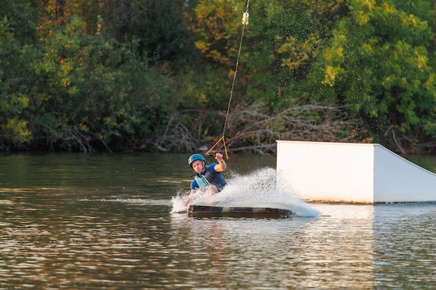 Sportowiec skacze nad wodą Wakeboard park o zachodzie słońca. Jeździec wykonuje trik na desce