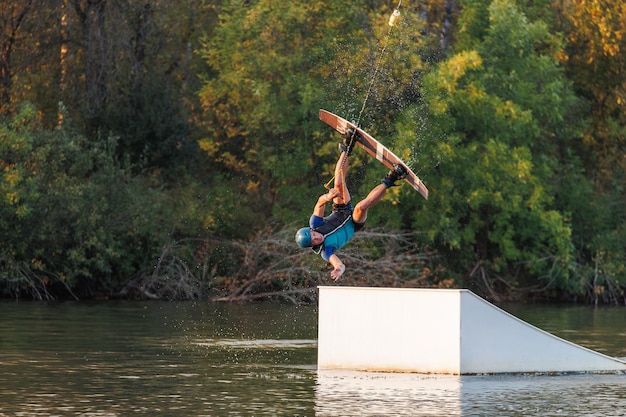 Sportowiec skacze z trampoliny Wakeboard park o zachodzie słońca Mężczyzna wykonuje trik na desce