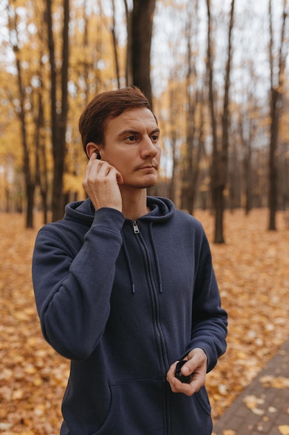 Sportowiec słuchający muzyki w słuchawkach przygotowujący się do treningu biegowego w jesiennym parku
