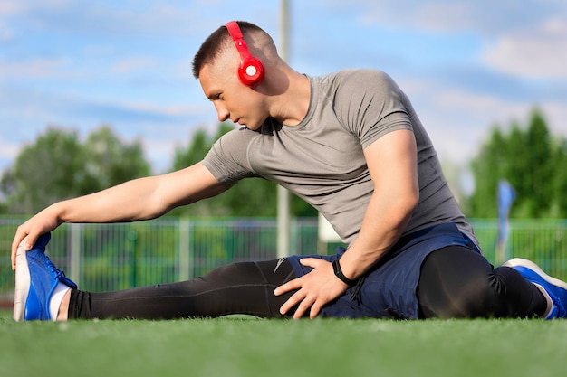 Sportowiec w niebieskich tenisówkach i sportowym mundurze wykonuje ćwiczenia rozciągające